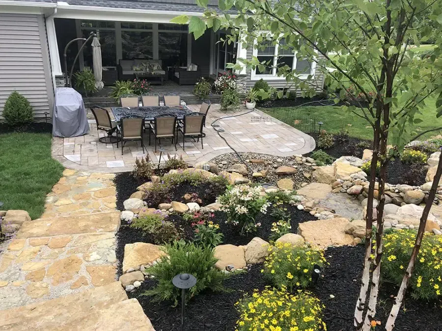 Backyard patio with outdoor dining set, stone walkway, and landscaped garden beds.