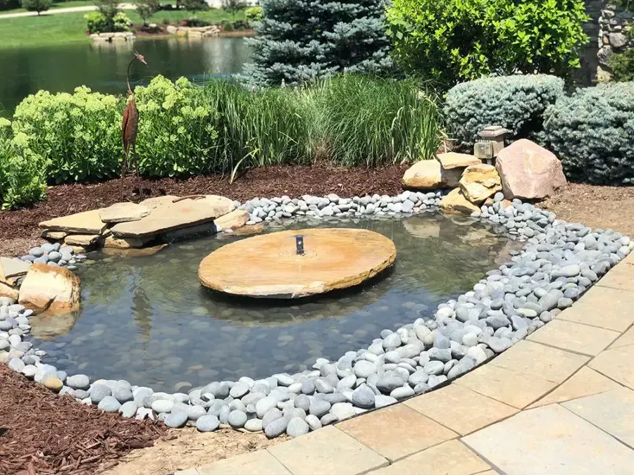 Garden pond with a small stone fountain, rocks, and lush greenery along the edge.