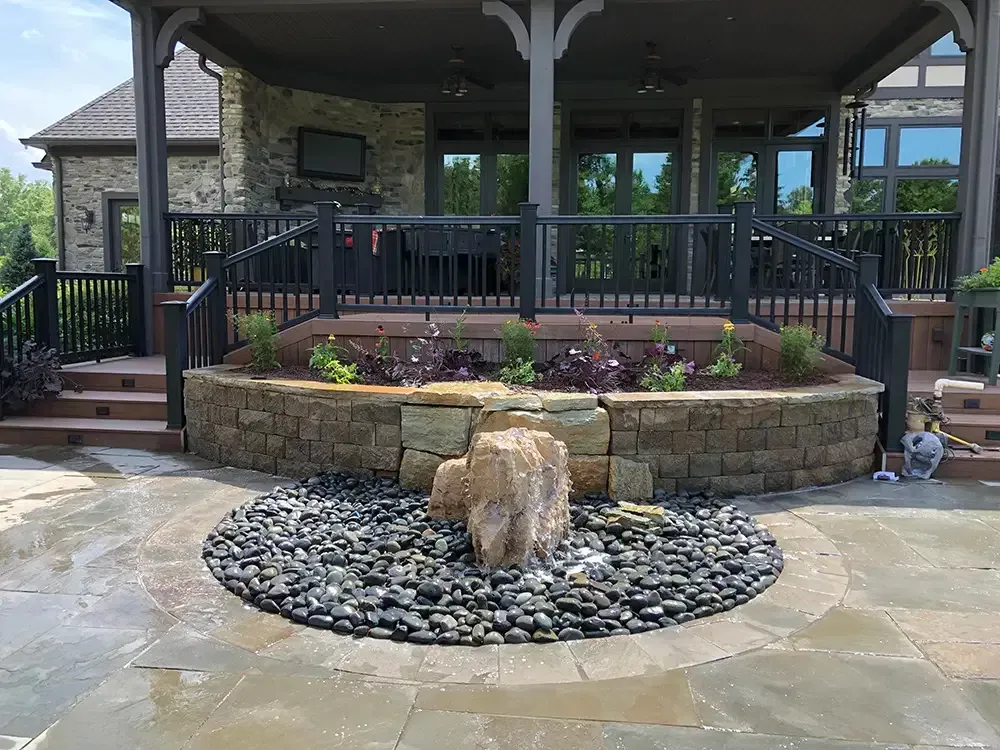Stone patio with a central rock garden and raised flower bed in front of a covered porch.
