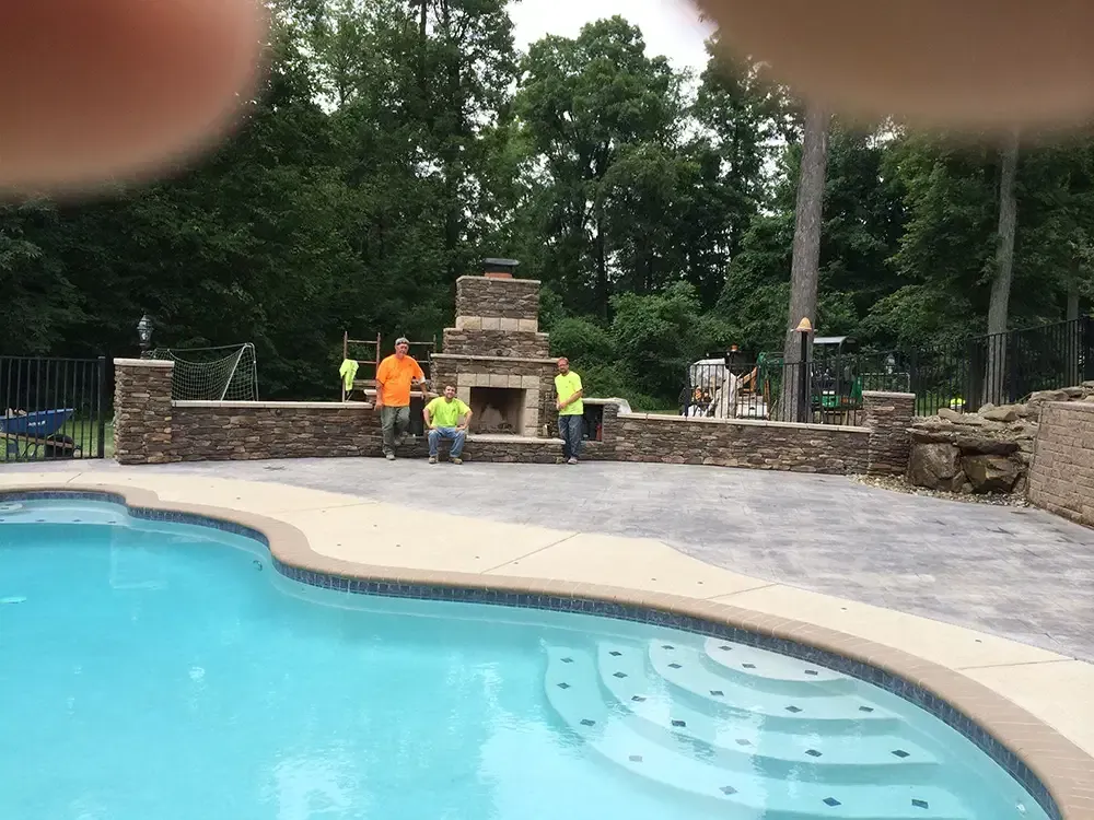 Backyard pool with workers repairing a stone patio and outdoor fireplace.