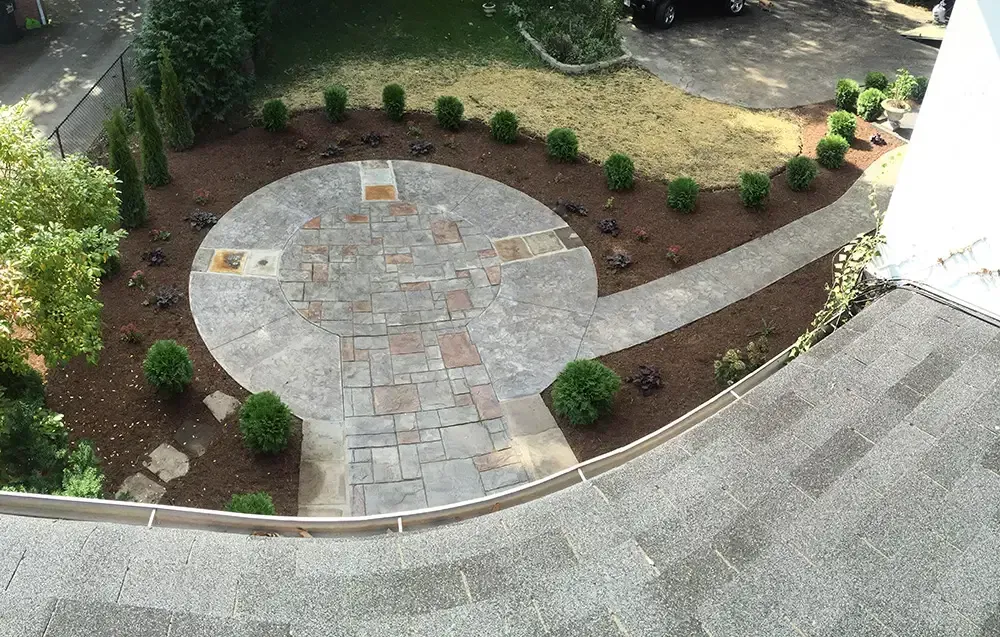 Stone patio with circular paving, curved walkway, and landscaped shrubs in a yard.