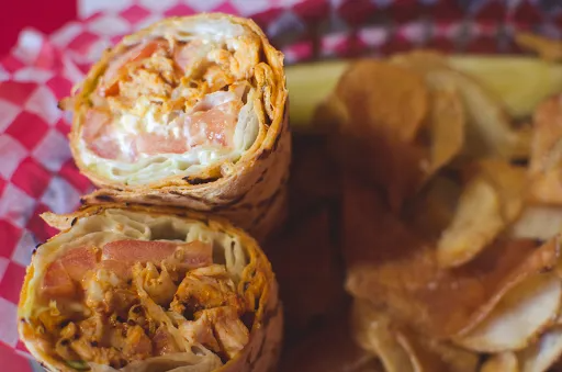 Chicken wrap with tomato and creamy sauce, served with chips and a pickle.