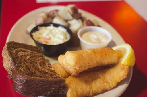 Plate of fried fish, bread, coleslaw, potatoes, and sauce on a red table.