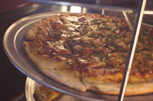 Pizza on a metal tray inside a warm oven, with visible melted cheese and toppings.