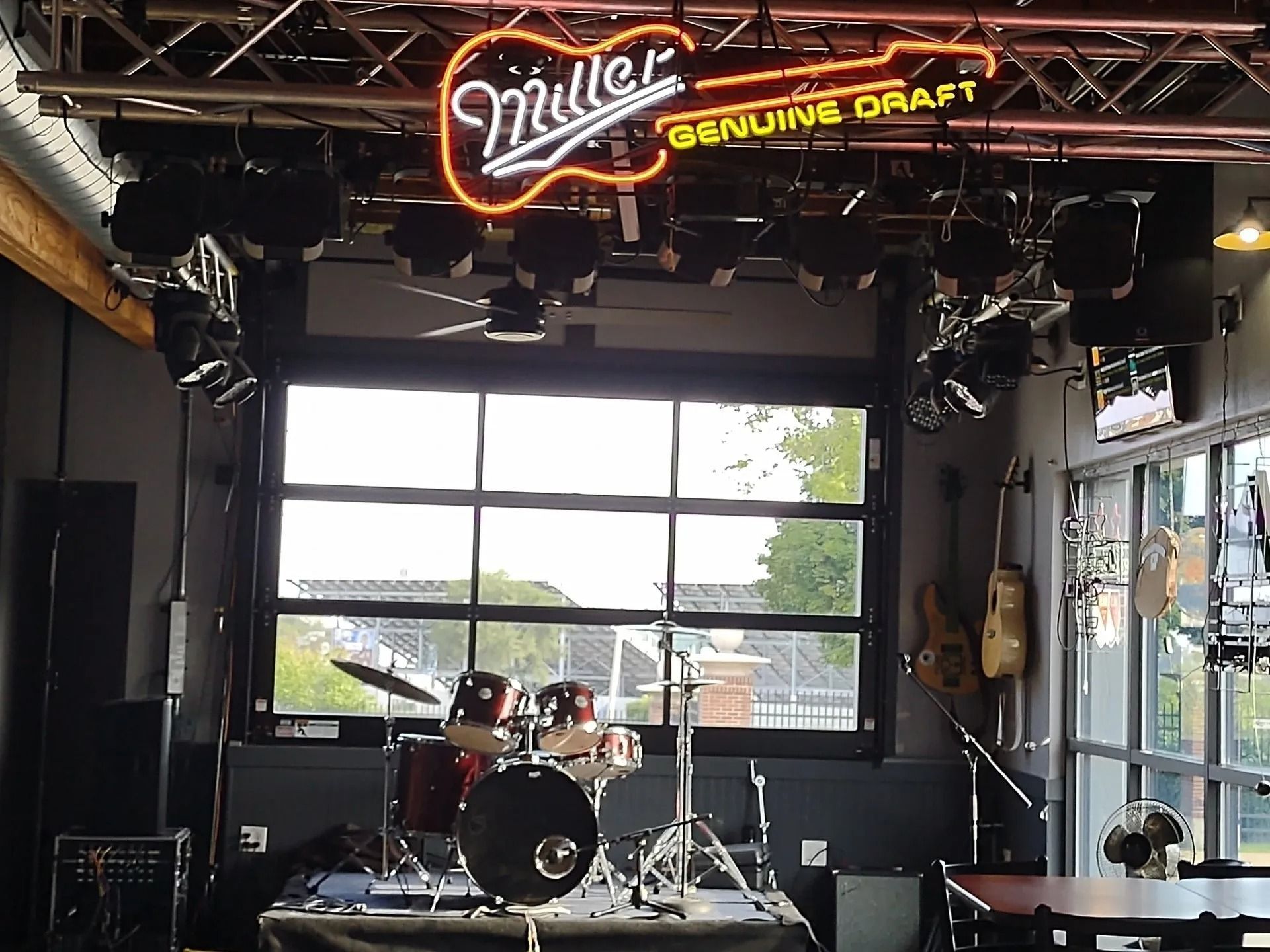 Stage setup in a bar with a Miller Genuine Draft neon sign, drums, and stage lights.