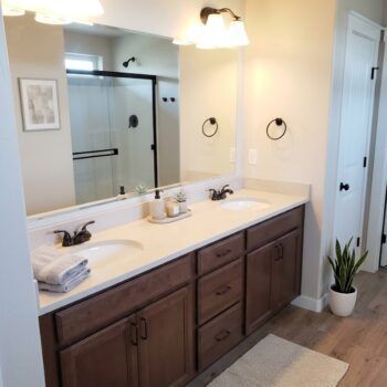 A modern double-sink bathroom vanity with dark wood cabinets, light countertops, and a large mirror.