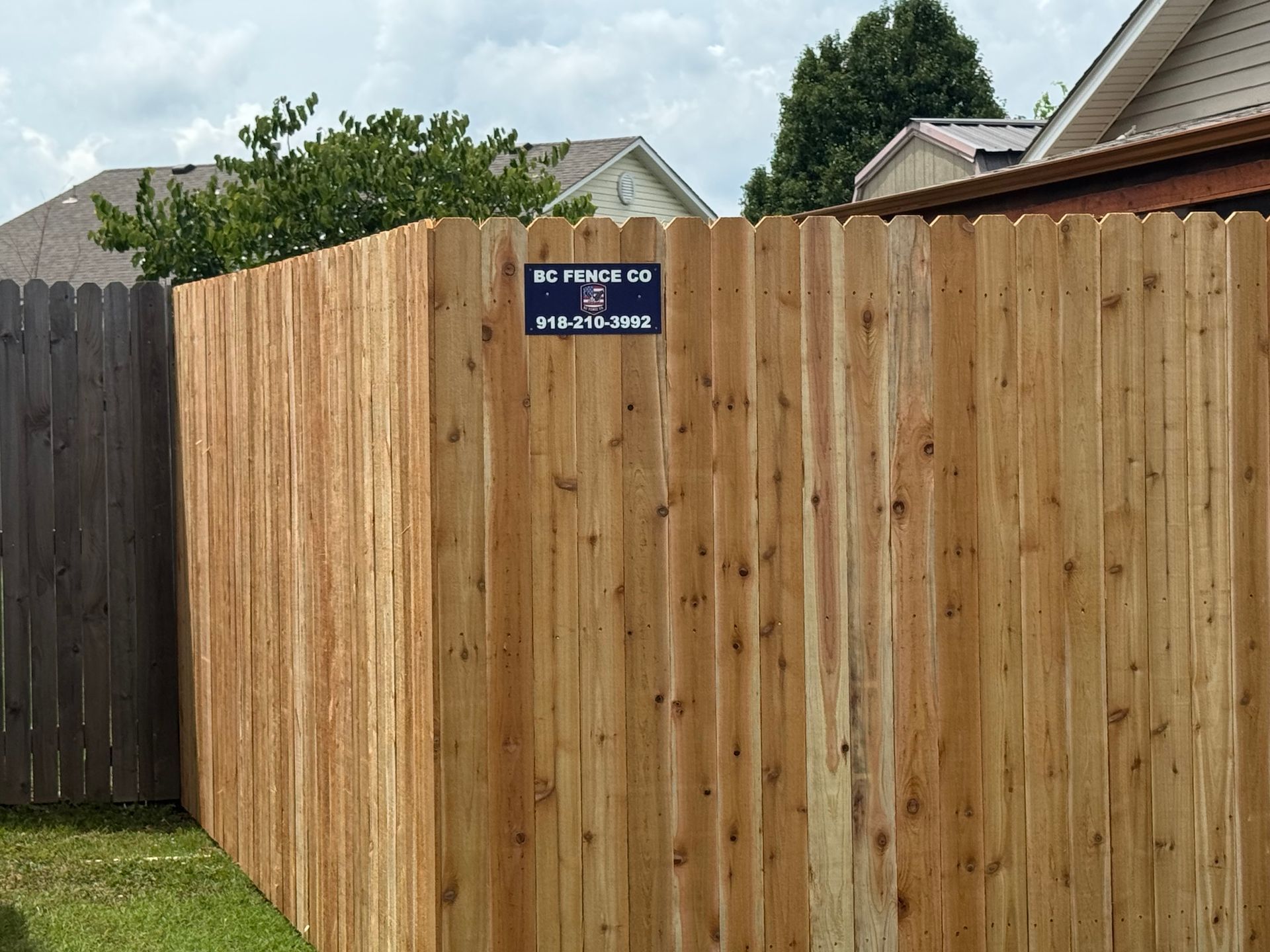 Wooden privacy fence corner with a blue security sign in a suburban yard.