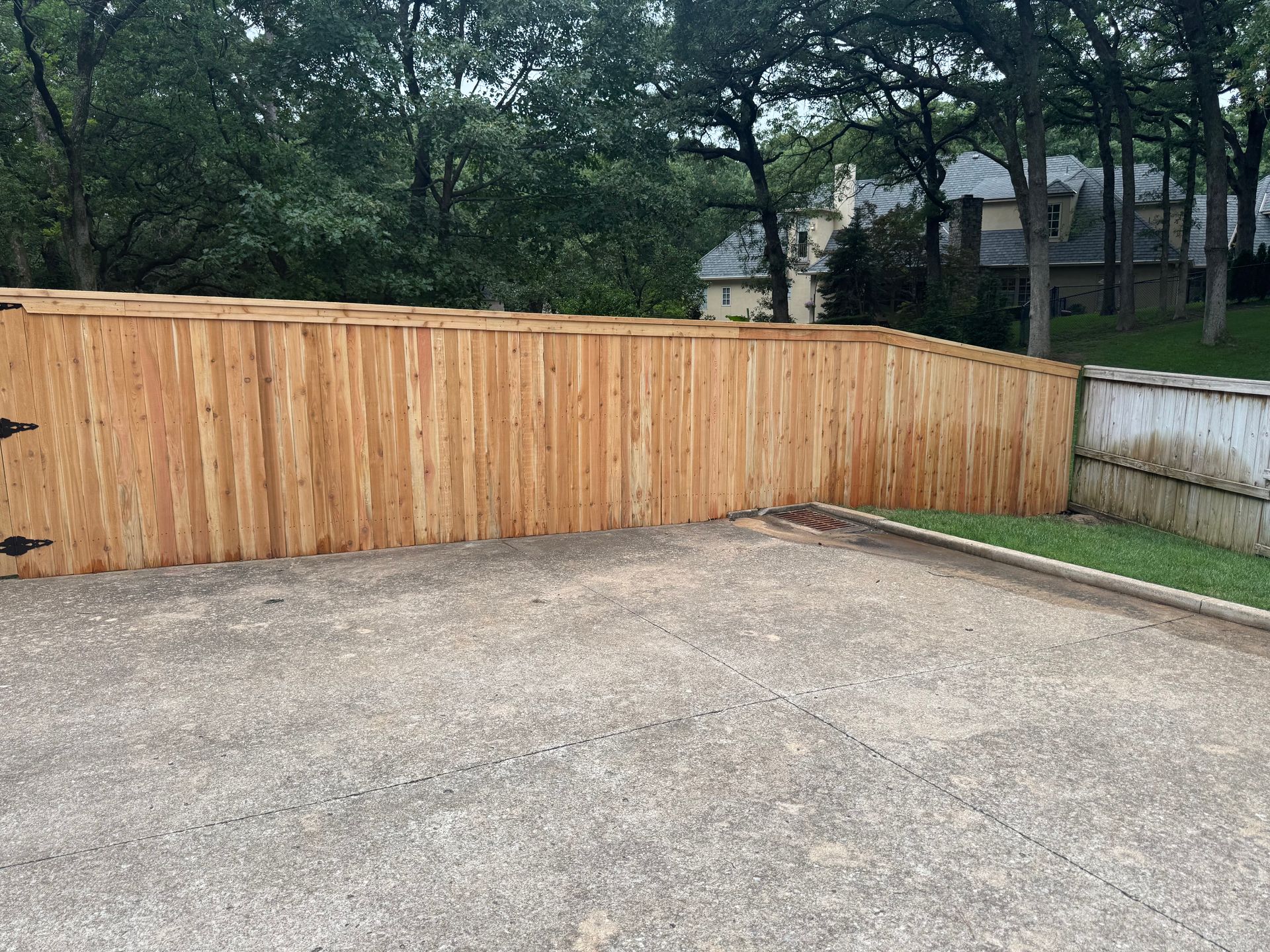 Gravel driveway beside a wooden privacy fence with trees and a house in the background