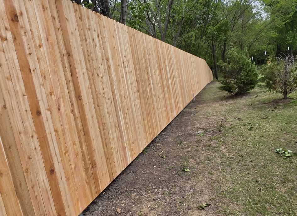 Wooden privacy fence along a grassy yard with trees in the background