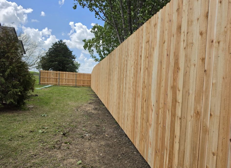 Wooden privacy fence along a grassy yard under a partly cloudy sky