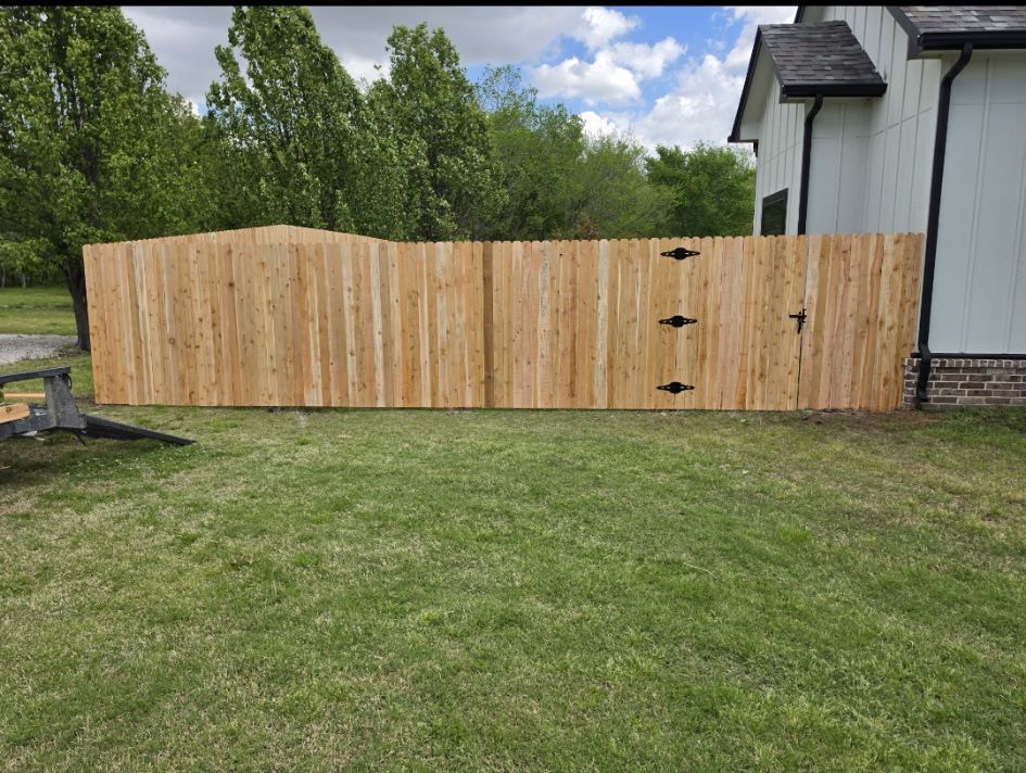 Wooden privacy fence with double gate in a grassy backyard beside a house and trees