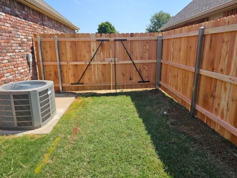 Backyard with grass, wooden fence and gate, and an air conditioner unit beside a brick house