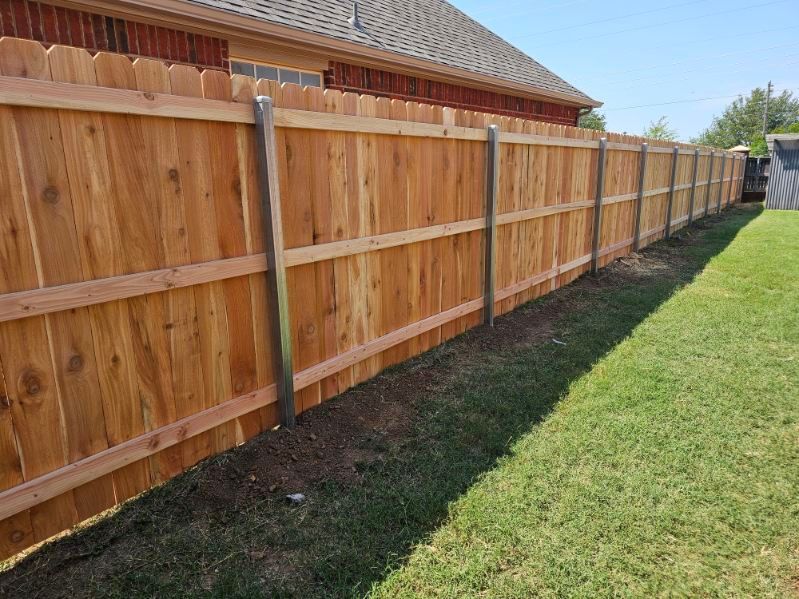 Wooden privacy fence beside a house, with green lawn and blue sky.
