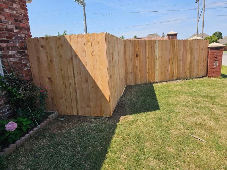 Wooden privacy fence enclosing a corner of a grassy backyard beside a brick house