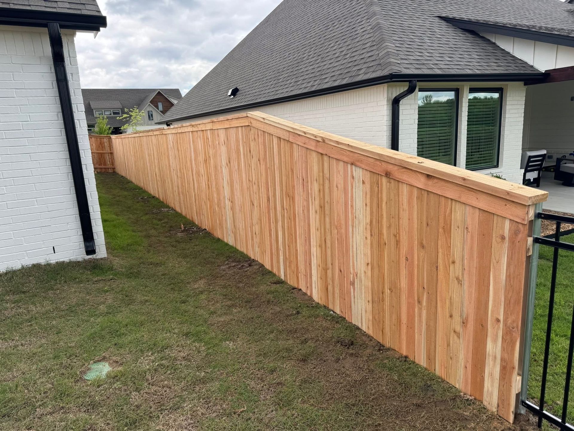 Long wooden privacy fence along a narrow grassy side yard beside two houses