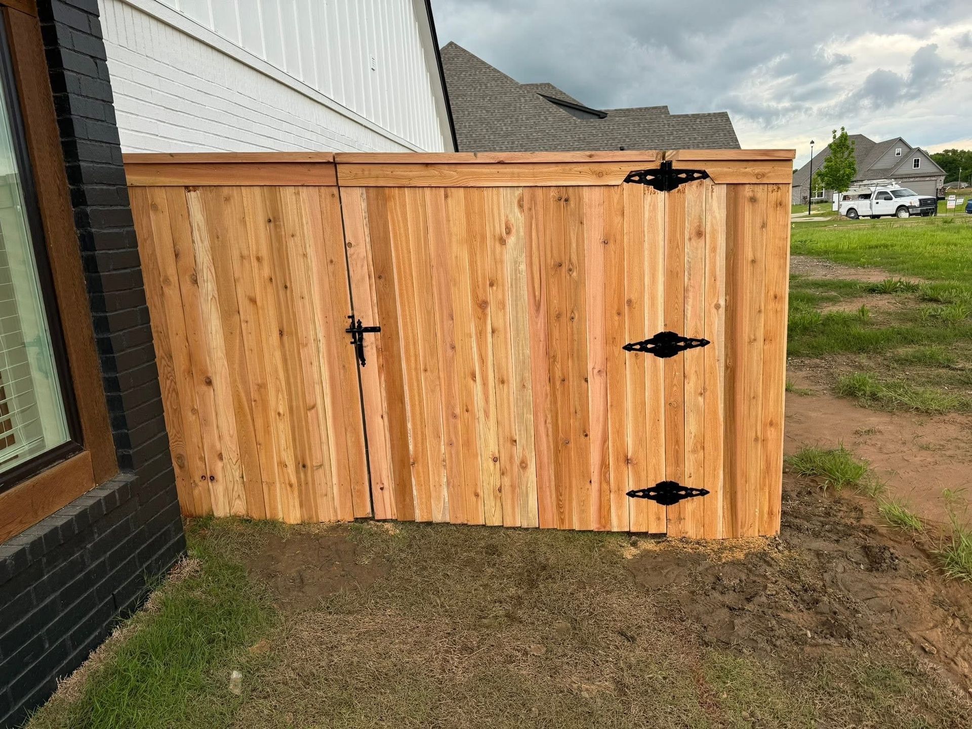 Wooden outdoor storage shed beside a house with black hinges on a grassy yard