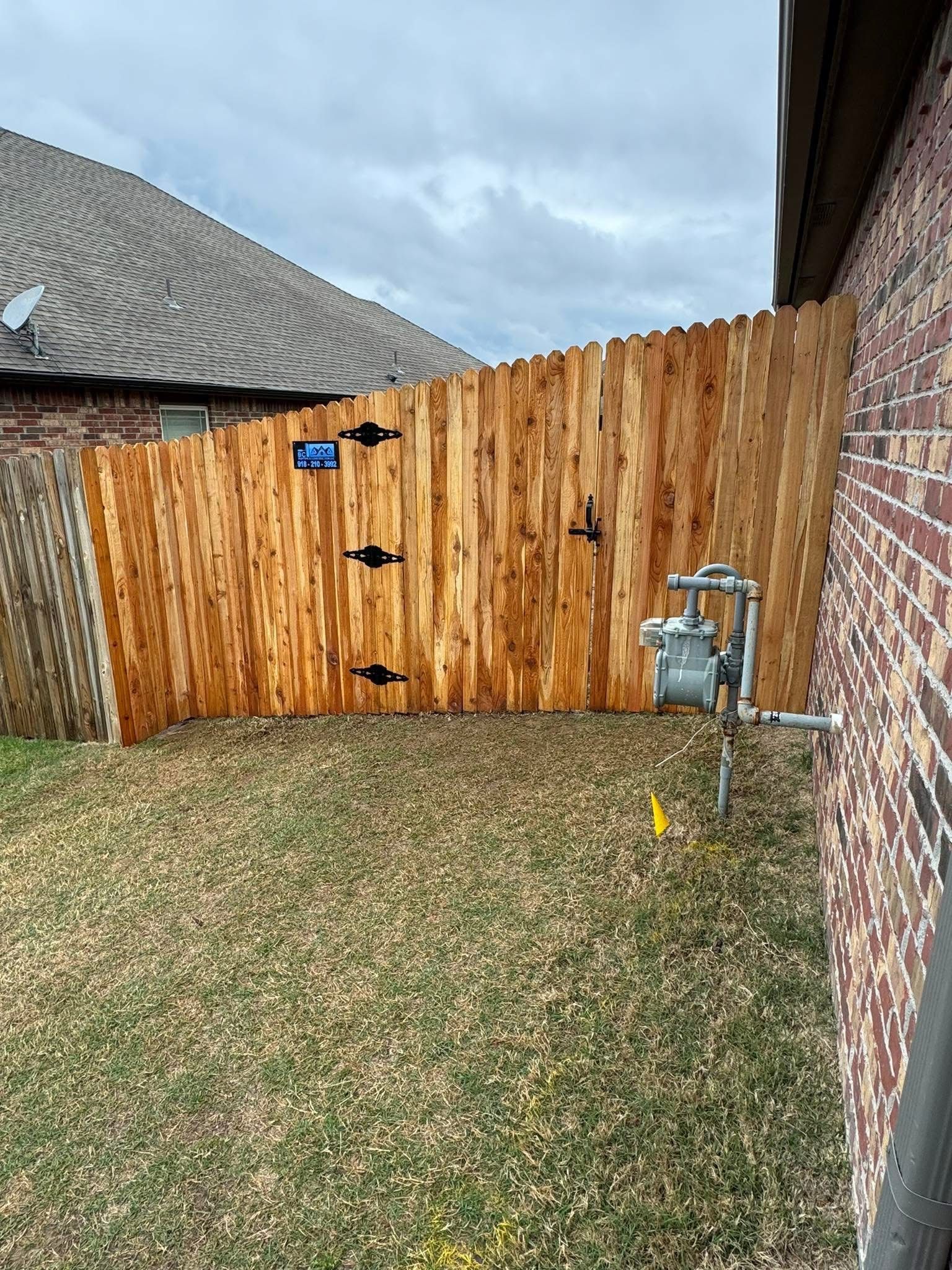 Backyard with wooden privacy fence, brick house wall, grass lawn, and a gas meter near the fence