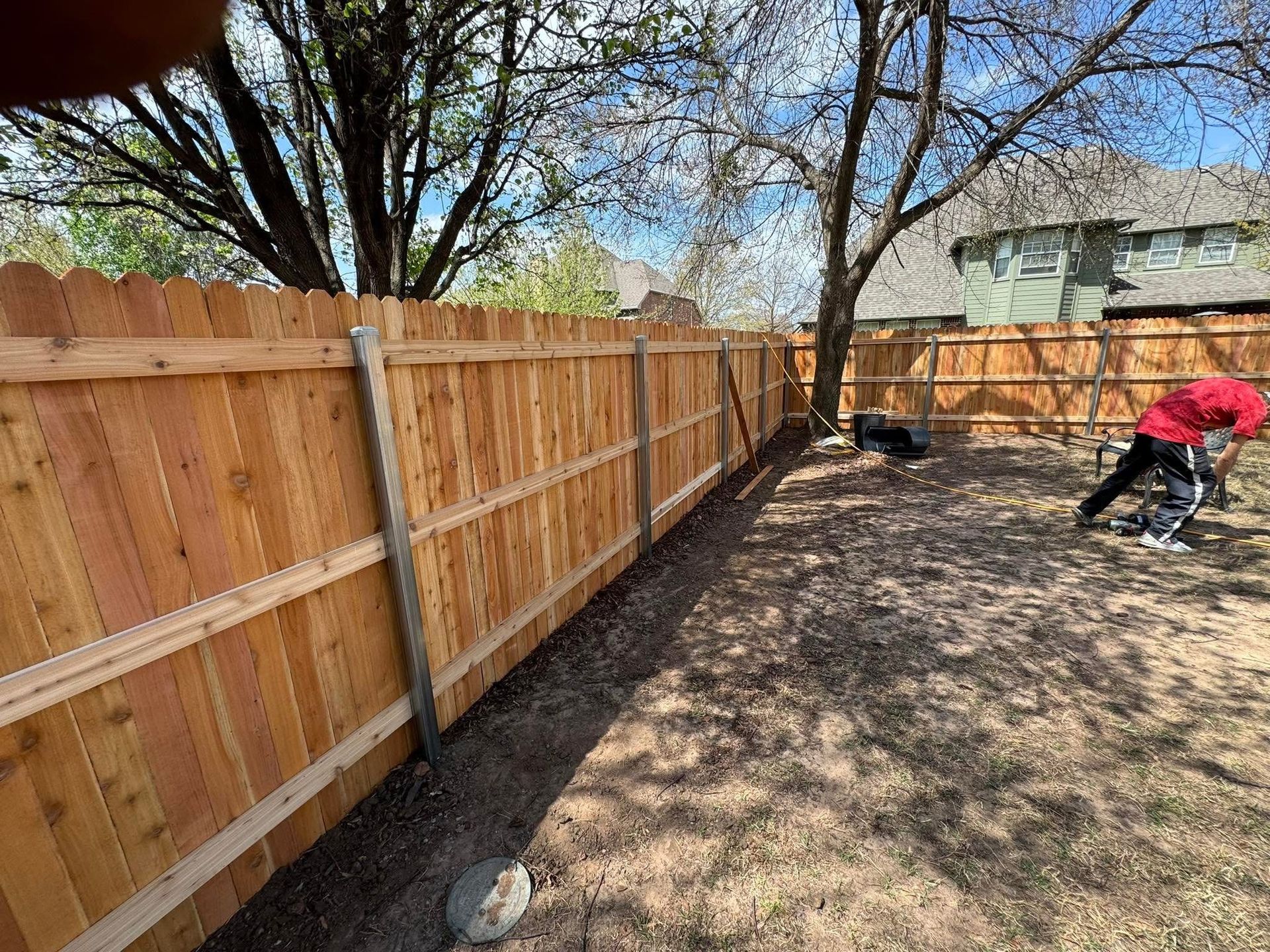 Wooden fenced yard with bare trees and a person working near the right side.