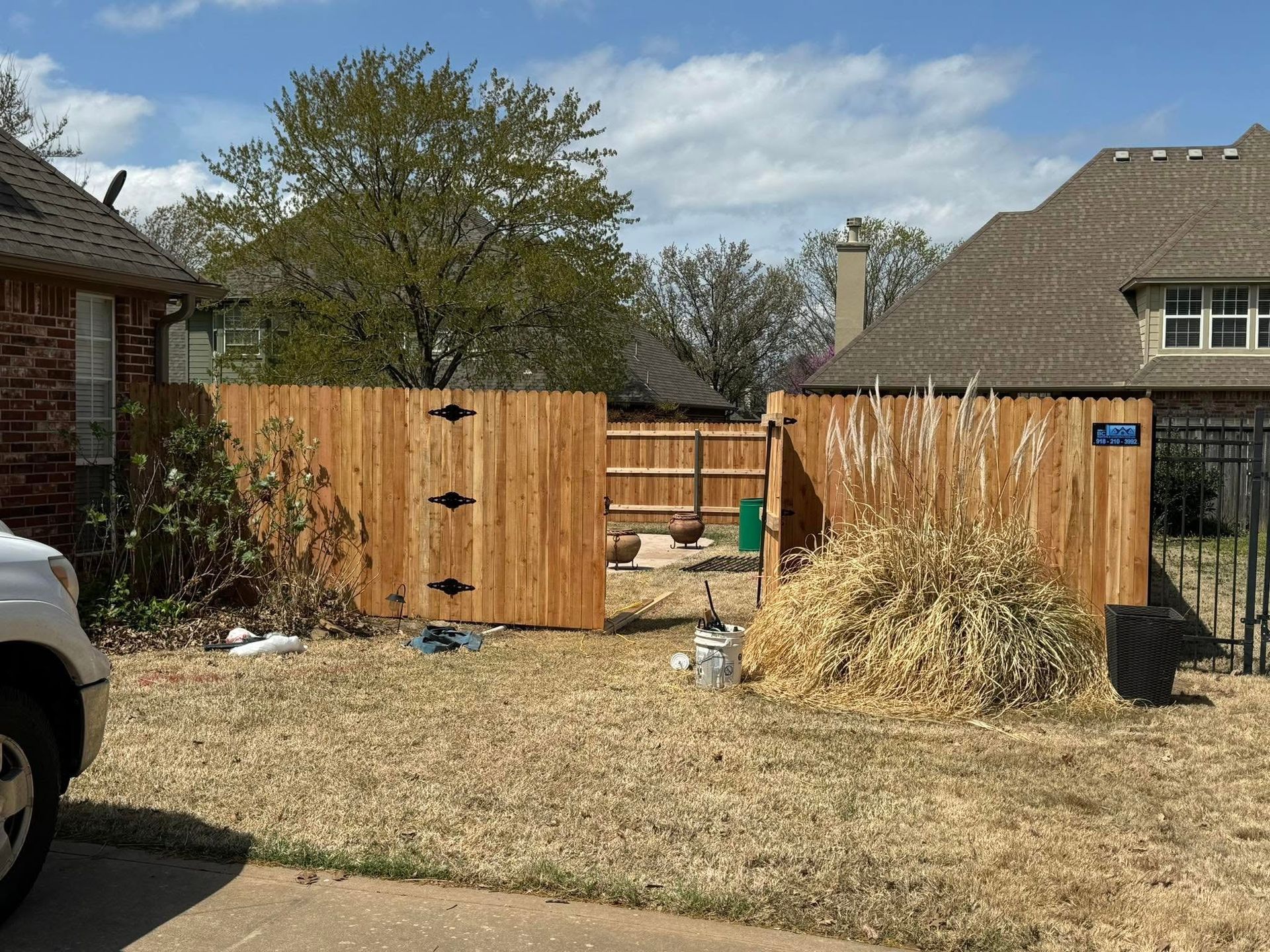 Backyard with wooden fence, dry grass, and a small gate between two houses under a blue sky