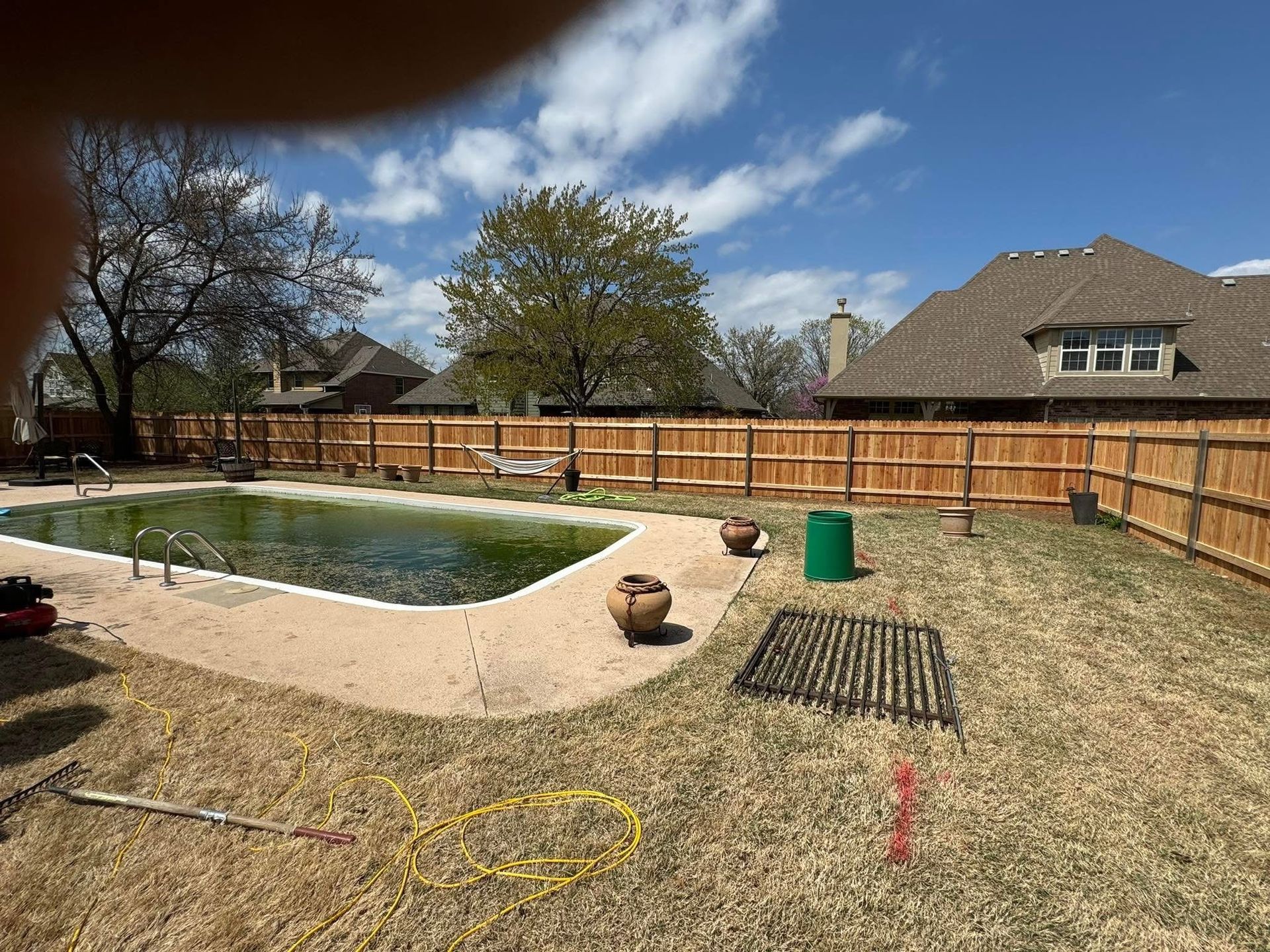 Backyard with a small pond, wooden fence, bare trees, and a suburban house under a blue sky