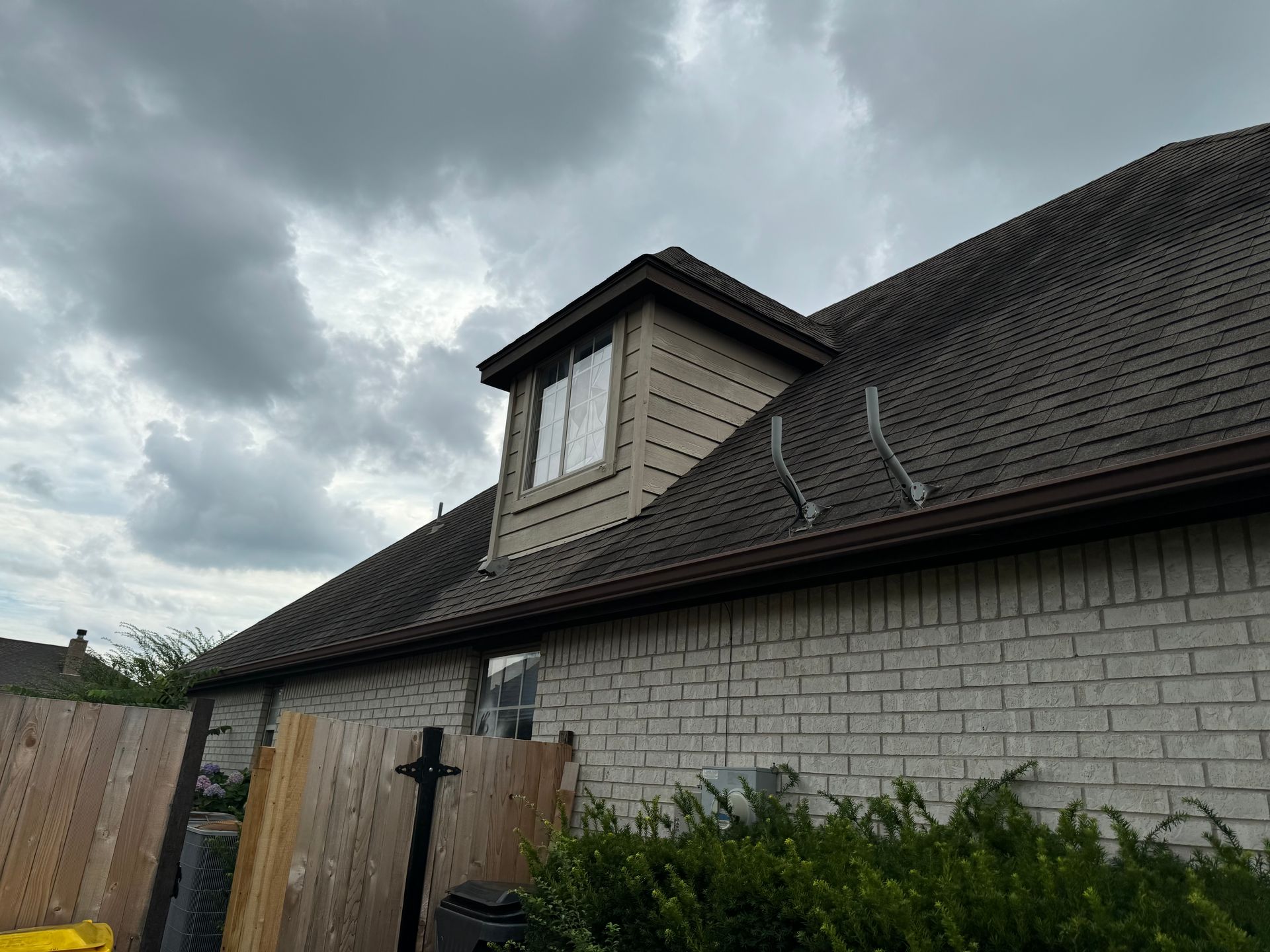 Gray brick house with a dark shingled roof and small dormer under cloudy skies