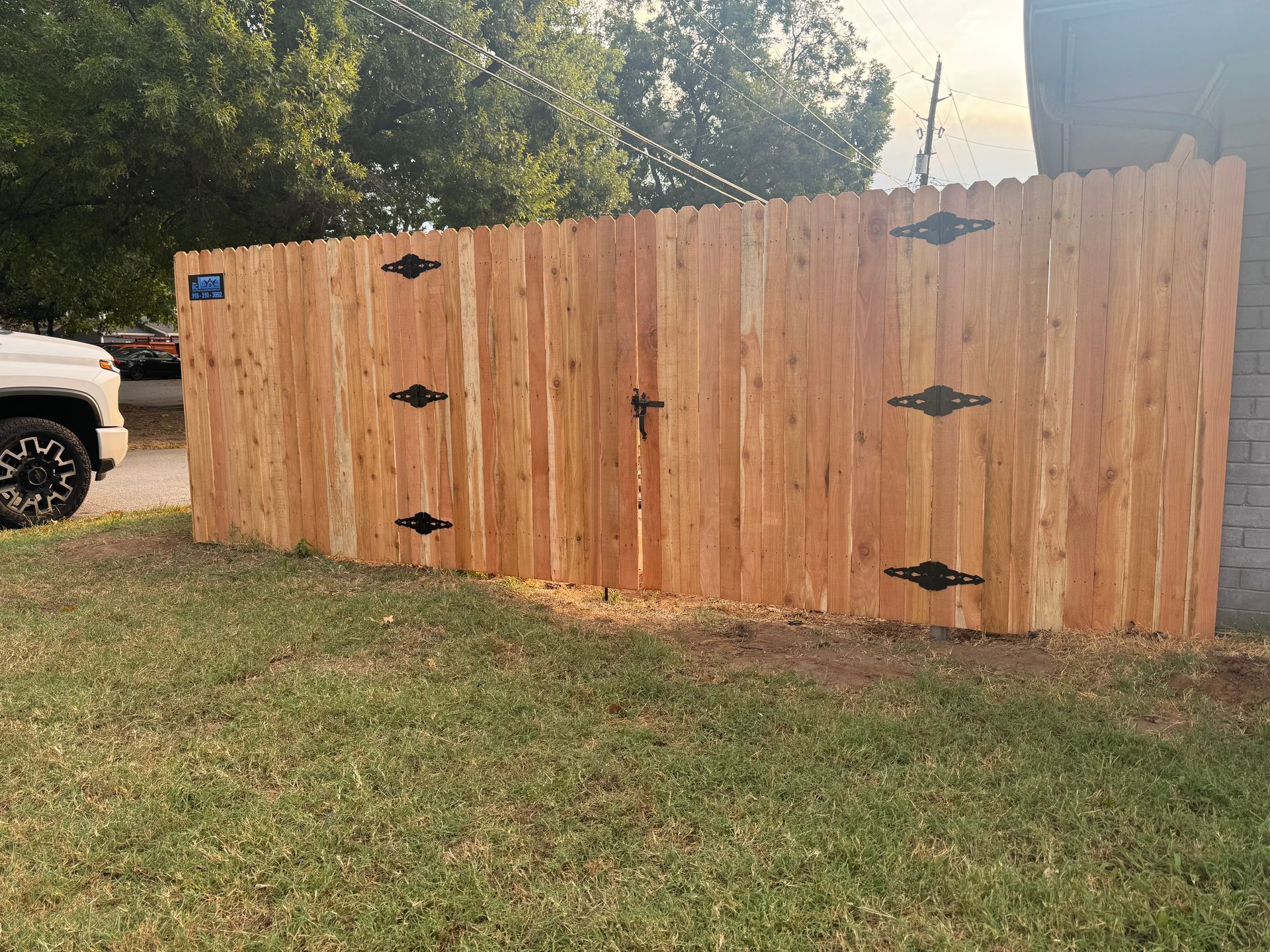 Wooden privacy fence with black hinges in a grassy yard beside a parked truck.
