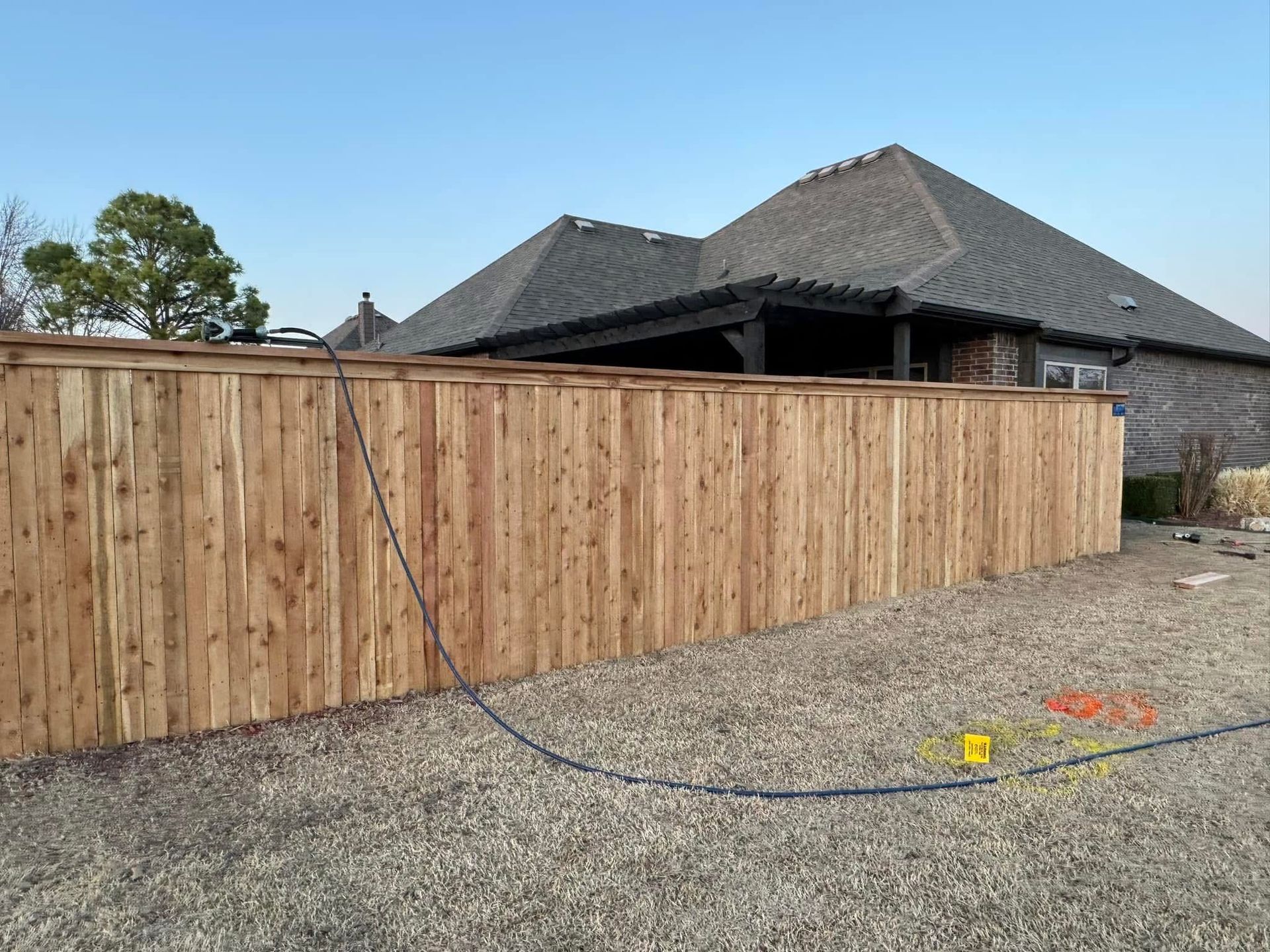 Wooden privacy fence in a gravel yard with a house behind it under a blue sky