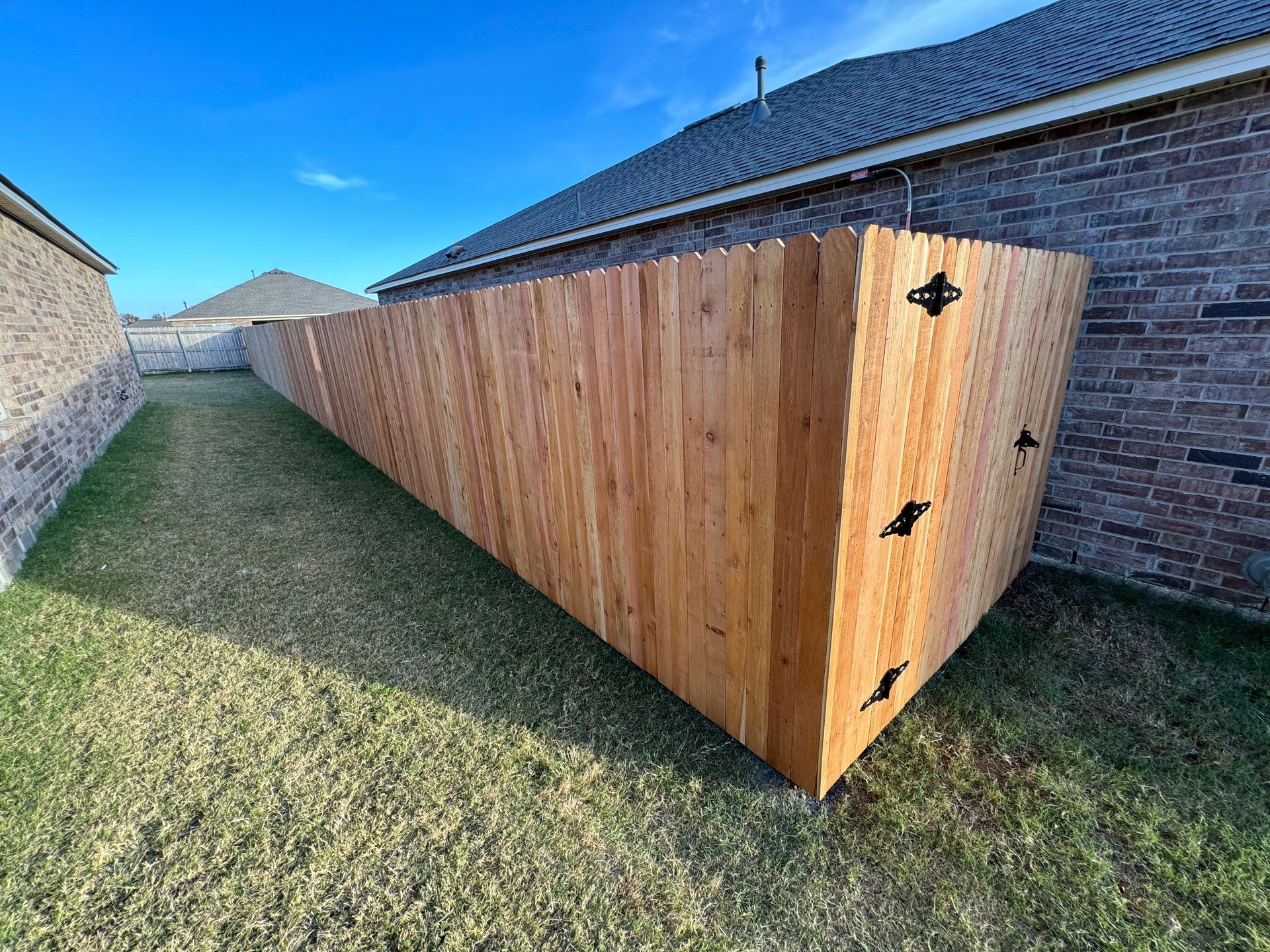 Long wooden fence beside a brick house along a narrow grassy side yard