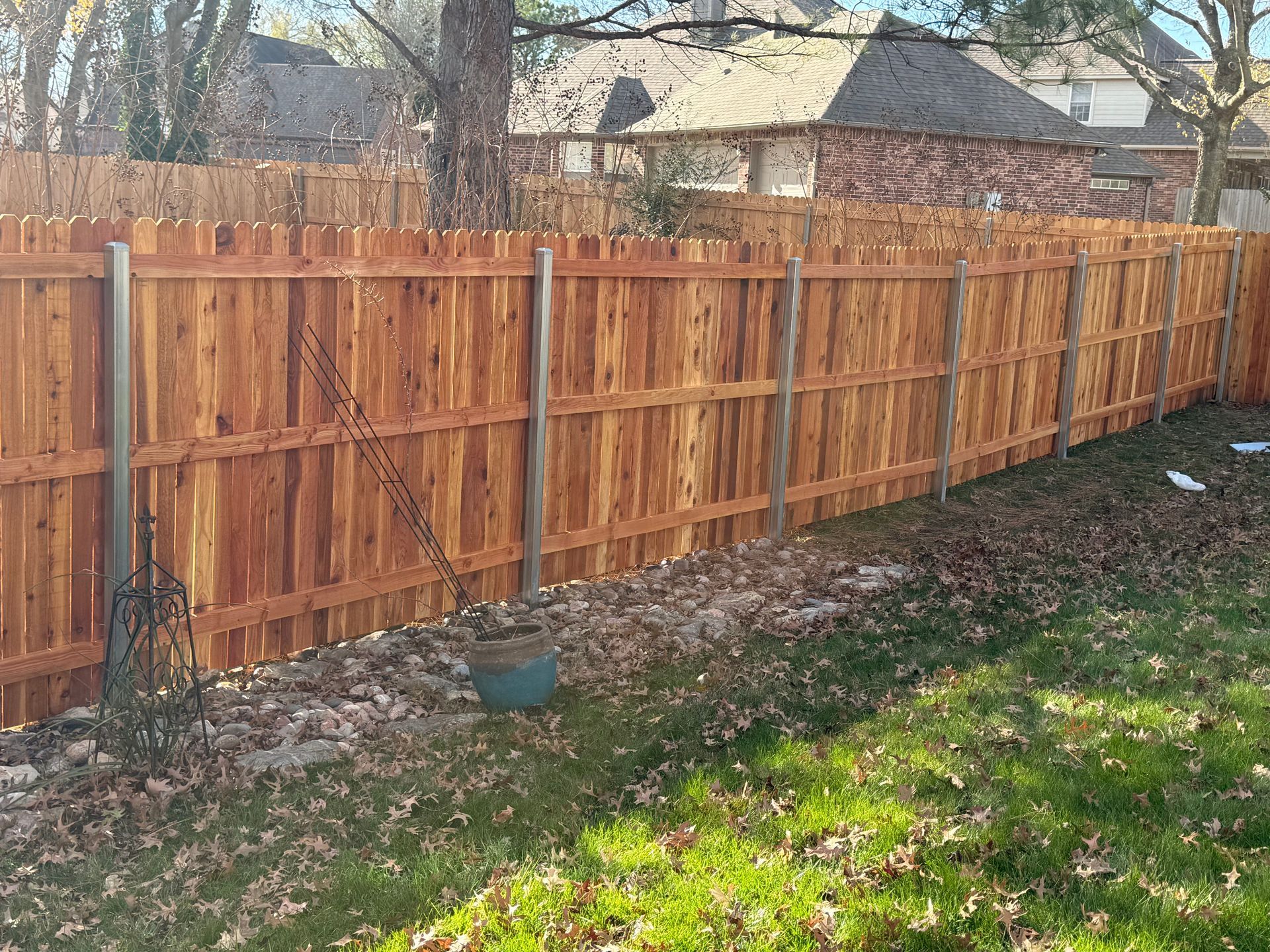 Wooden privacy fence along a backyard edge with fallen leaves and green grass in sunlight
