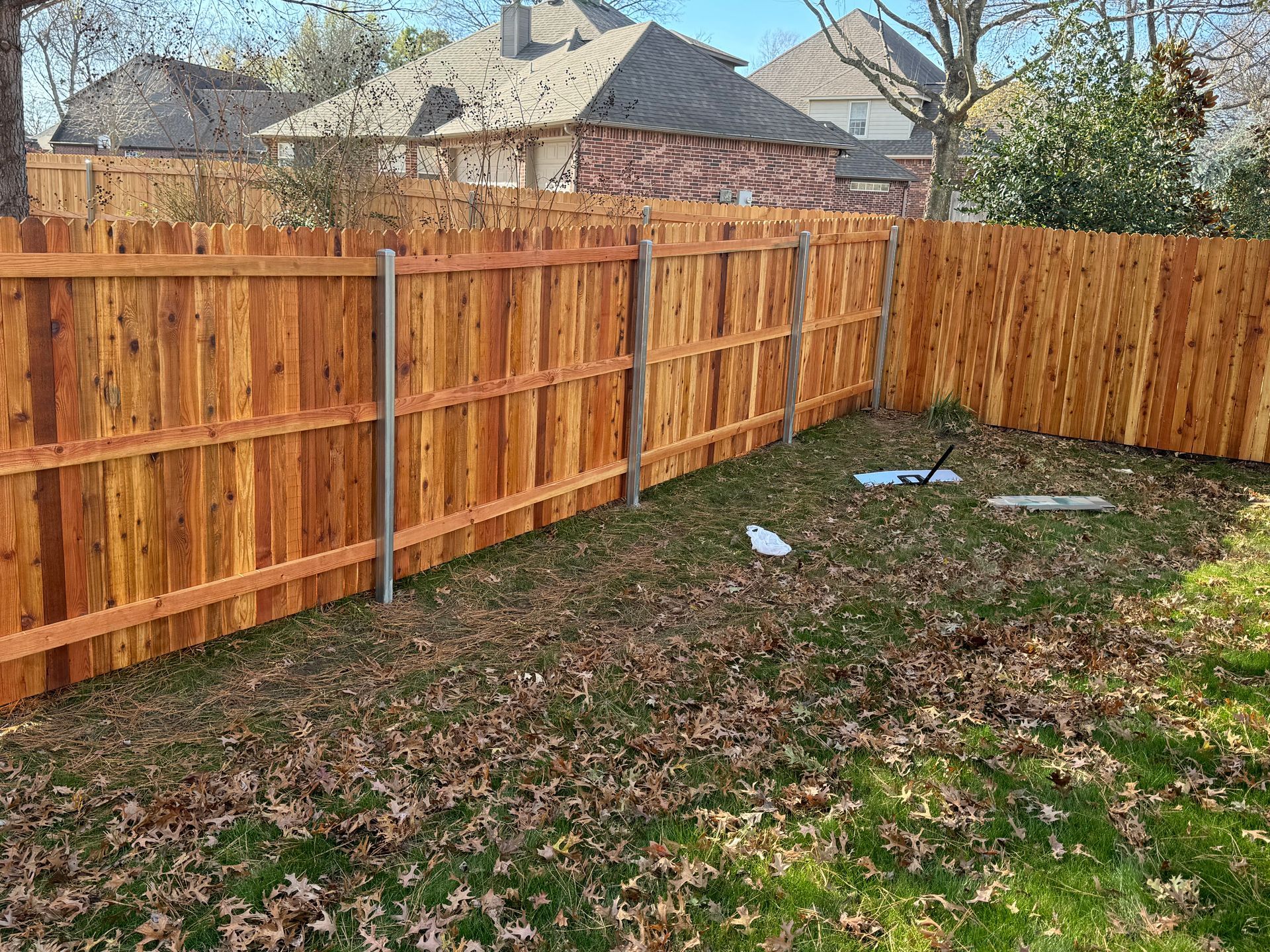 Backyard with a new wooden privacy fence and patchy grass under a sunny sky