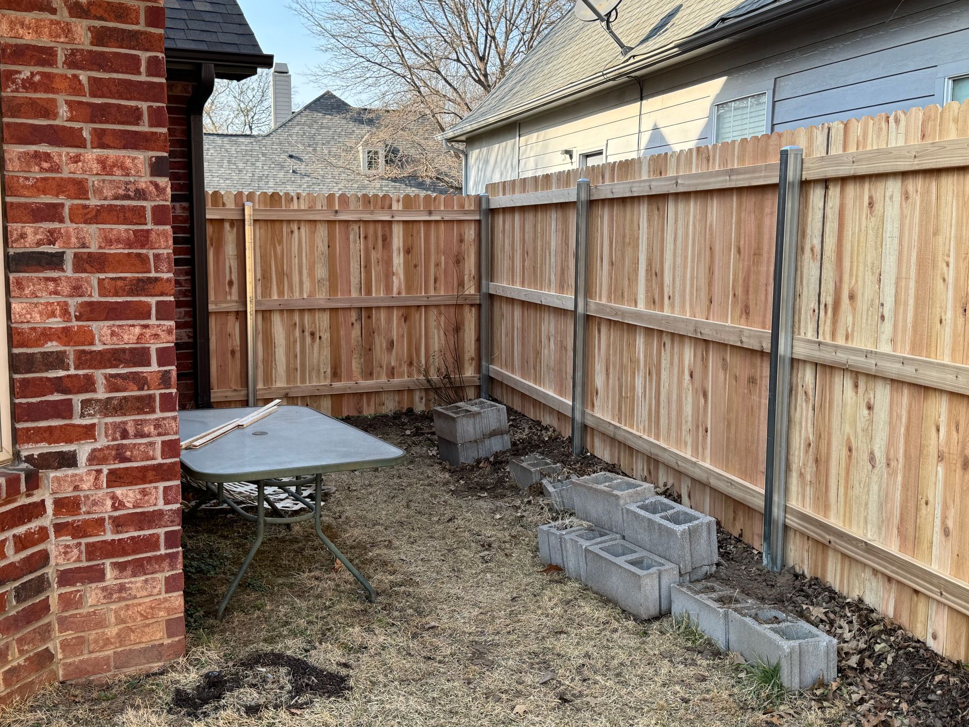 Small fenced backyard with a brick wall, round table, and stacked cinder blocks along the fence.