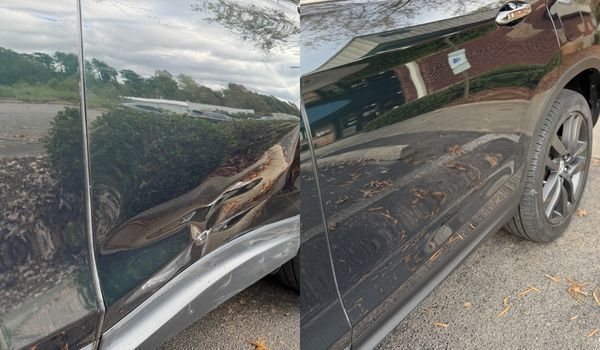 Damaged dark-colored car door with a dent. Reflection of environment visible.