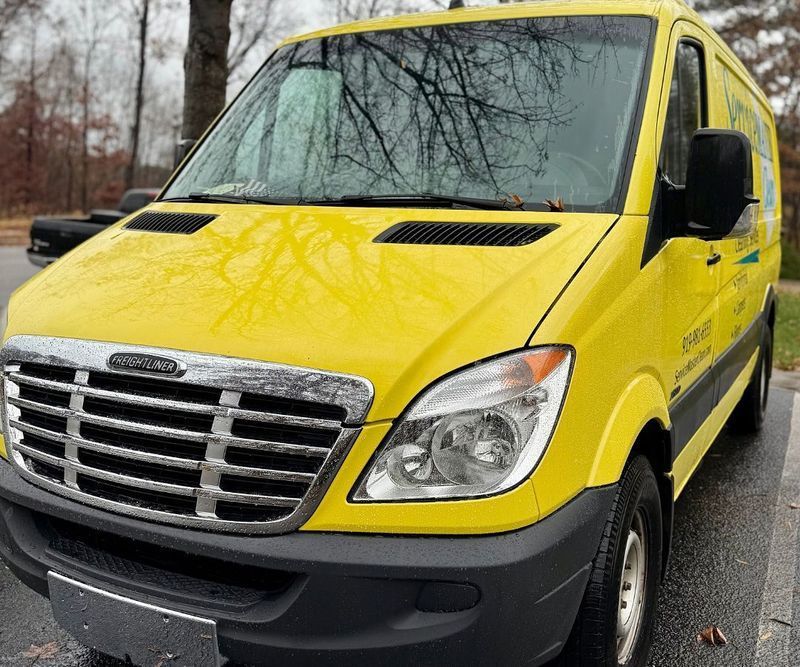 Yellow Freightliner Sprinter van with black trim parked outdoors.
