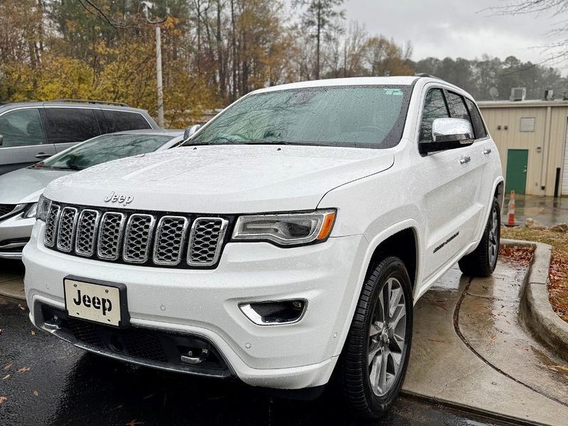 White Jeep Grand Cherokee SUV parked outdoors with wet pavement and a building in the background.