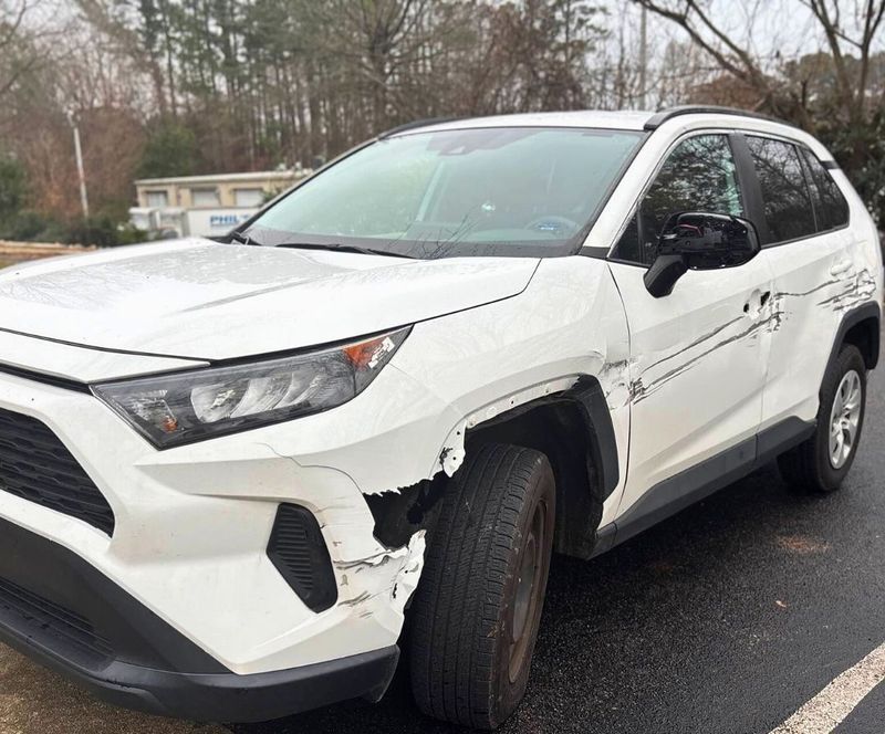 White Toyota SUV with front-end damage; parked on asphalt in front of a building.