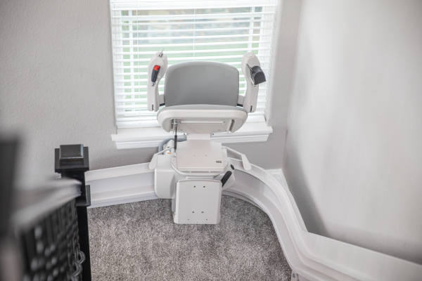Motorized stair lift in a bright room with a window and white railings.