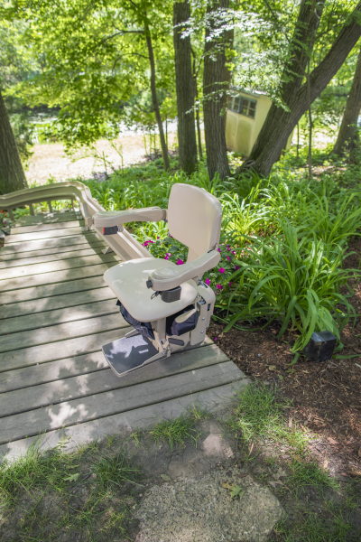 White outdoor chair on a wooden deck beside a lush garden path and trees.