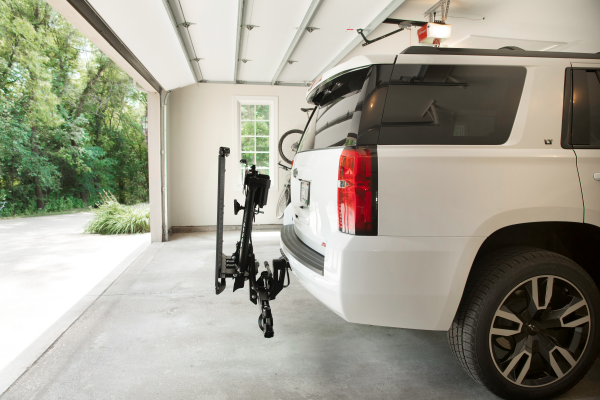 White SUV parked in a garage with a hitch-mounted bike rack extended at the rear.