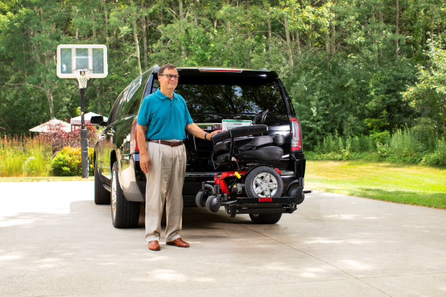 Man standing beside a black off-road vehicle with a mounted pressure washer on a driveway.