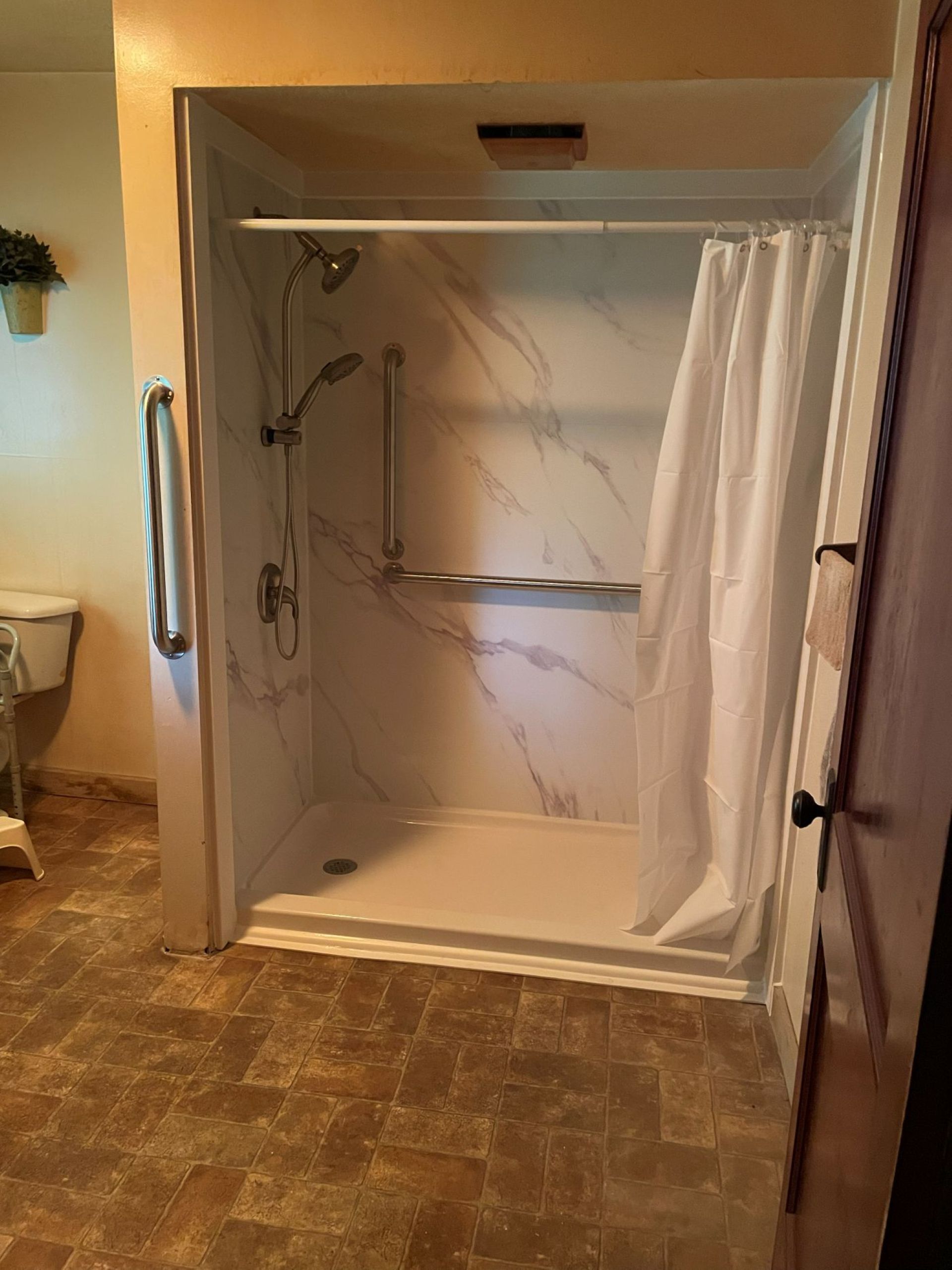 Bathroom shower with white curtain, built-in shelves, and beige tile floor.