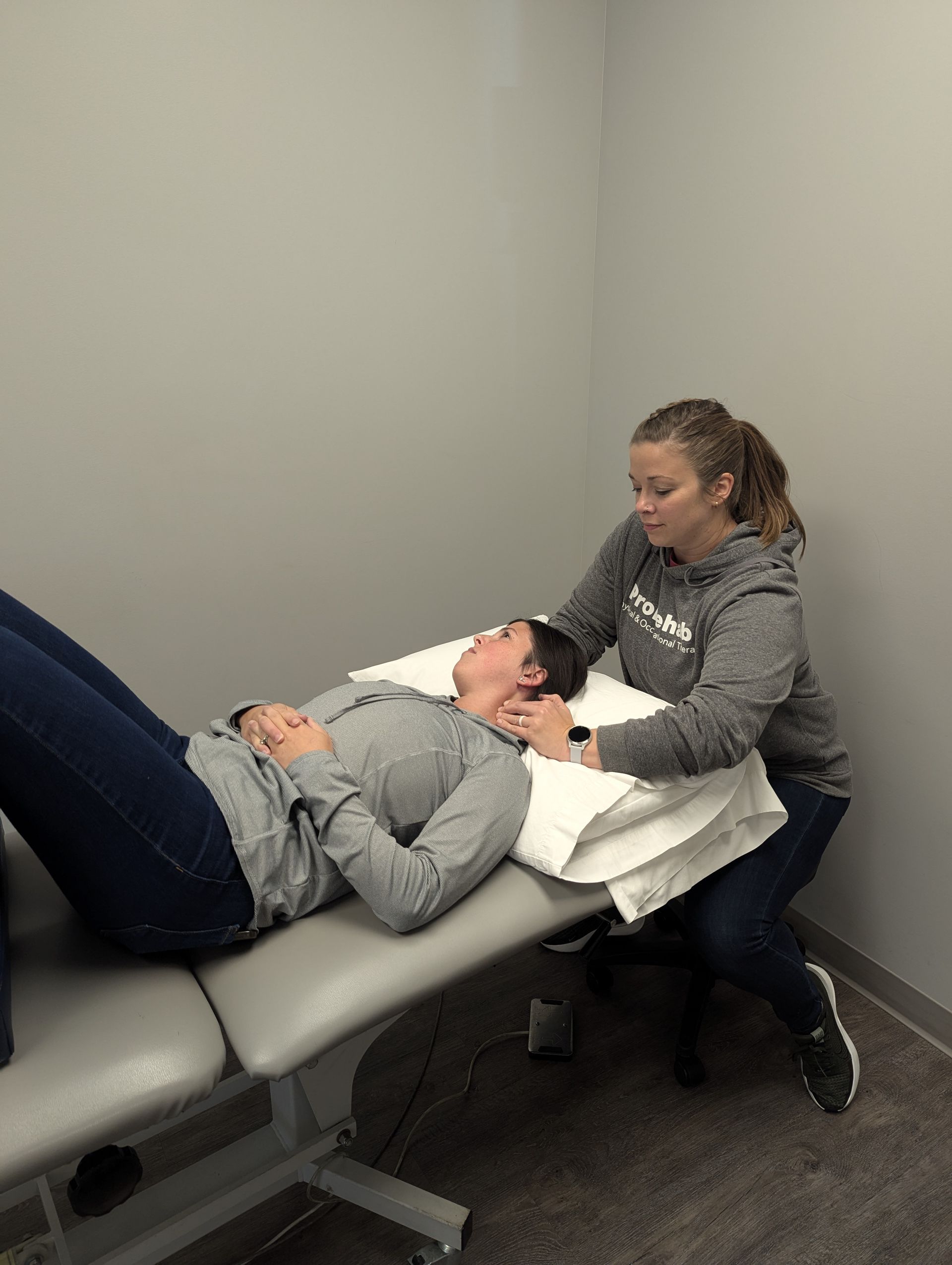 Woman receiving neck therapy from a person in a gray sweatshirt on a treatment table.
