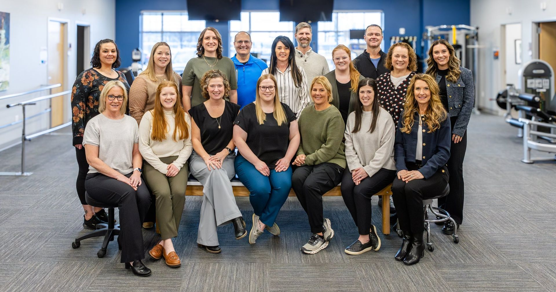 Group photo of a team in a physical therapy clinic. People are smiling, wearing casual work attire.