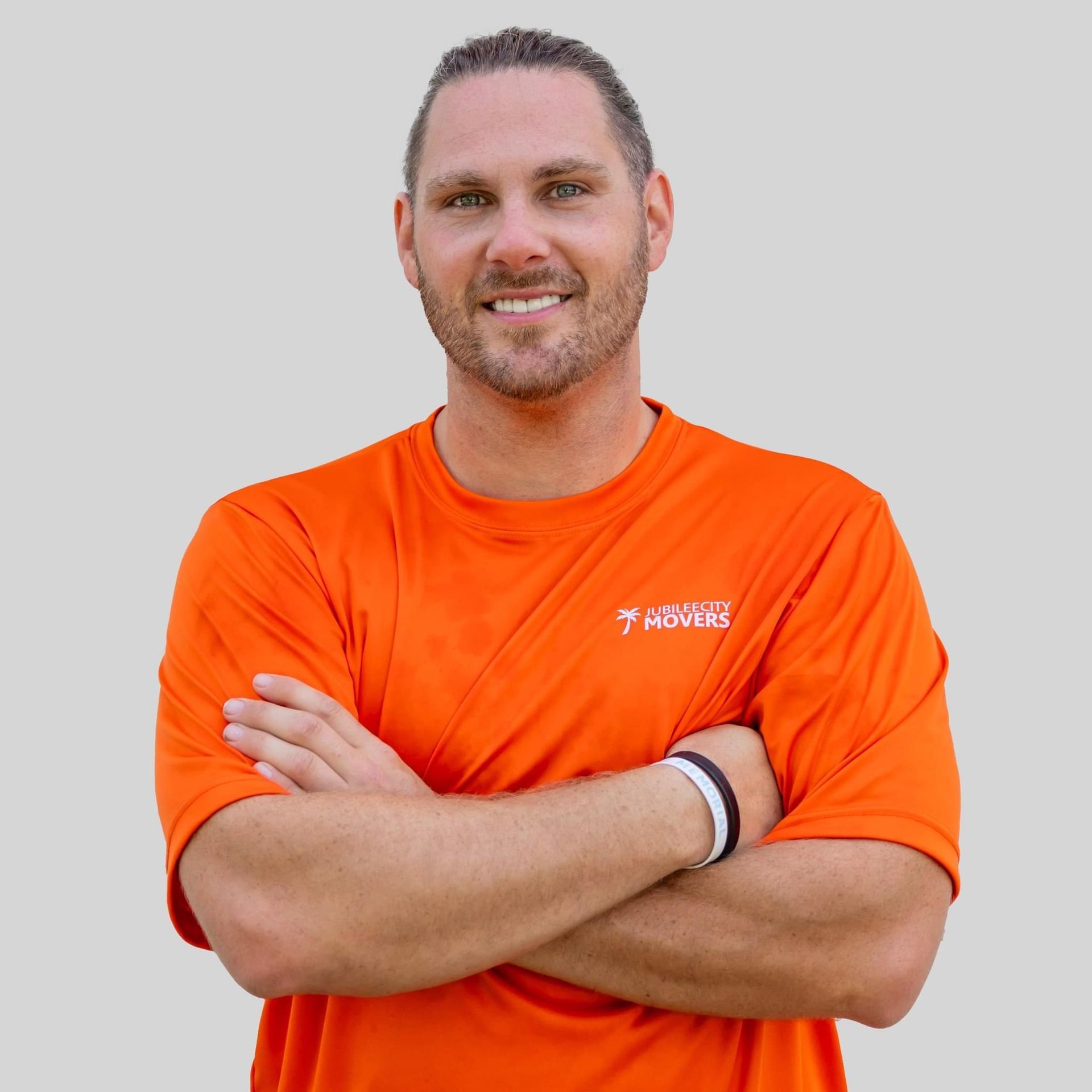 Man in an orange shirt with arms crossed, smiling.