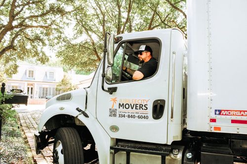 Moving truck with Liberty Movers logo, driver at the wheel, parked in front of the house.