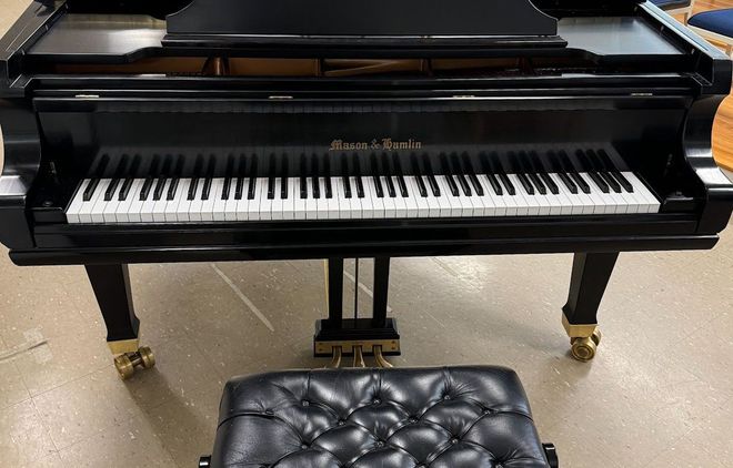 A black grand piano with a tufted black bench sits on a tan floor.