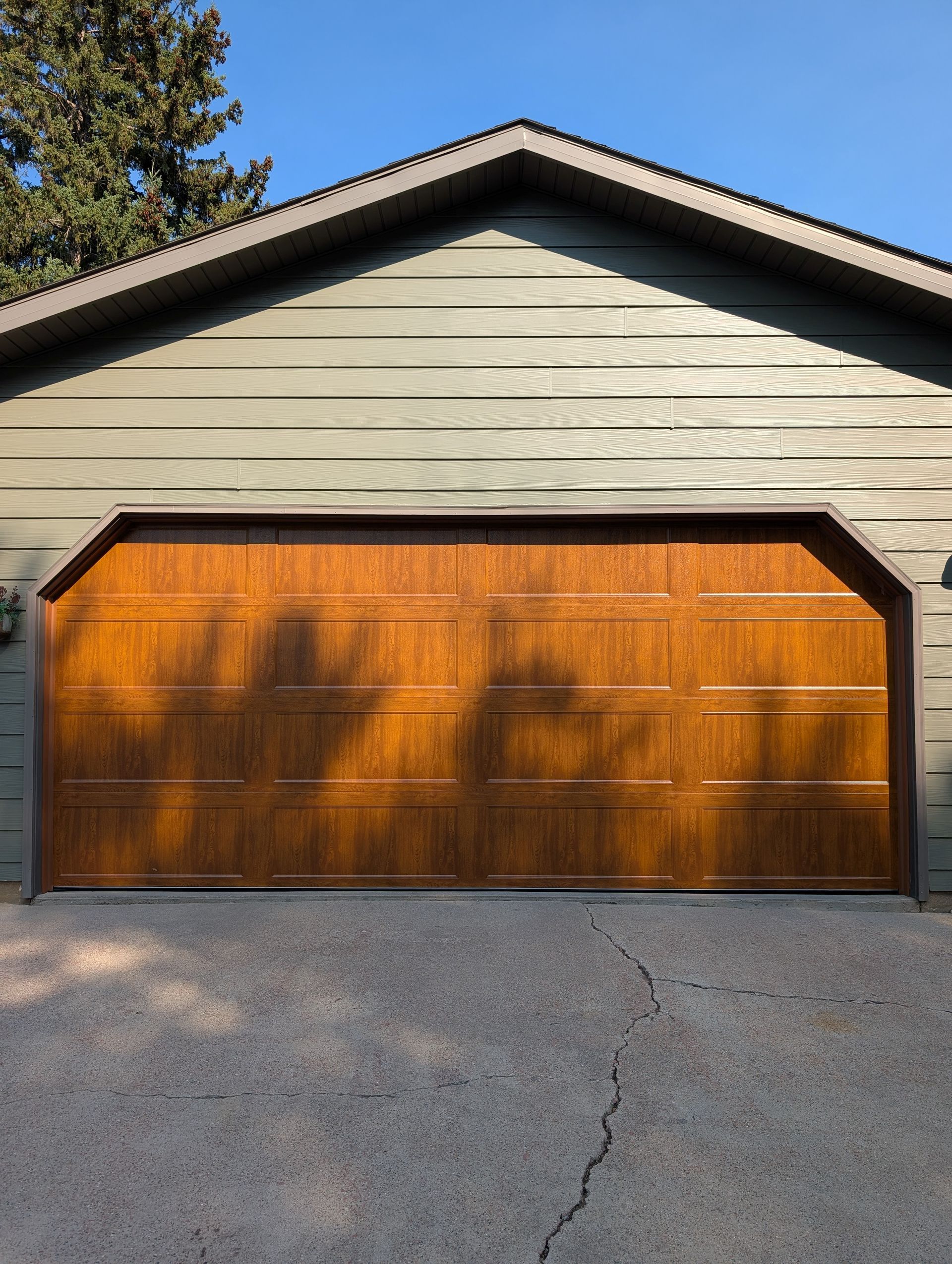 Wooden double garage door on a beige house with a gravel driveway and sunlit shadows