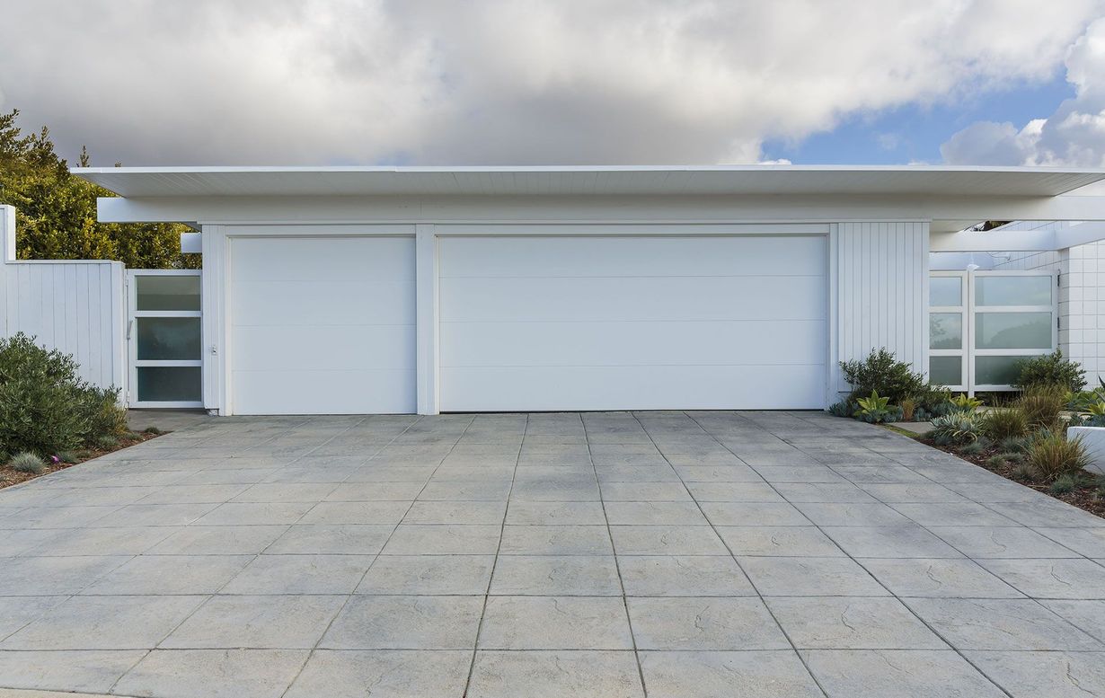 White garage with two doors and flat roof, concrete driveway, and overcast sky.