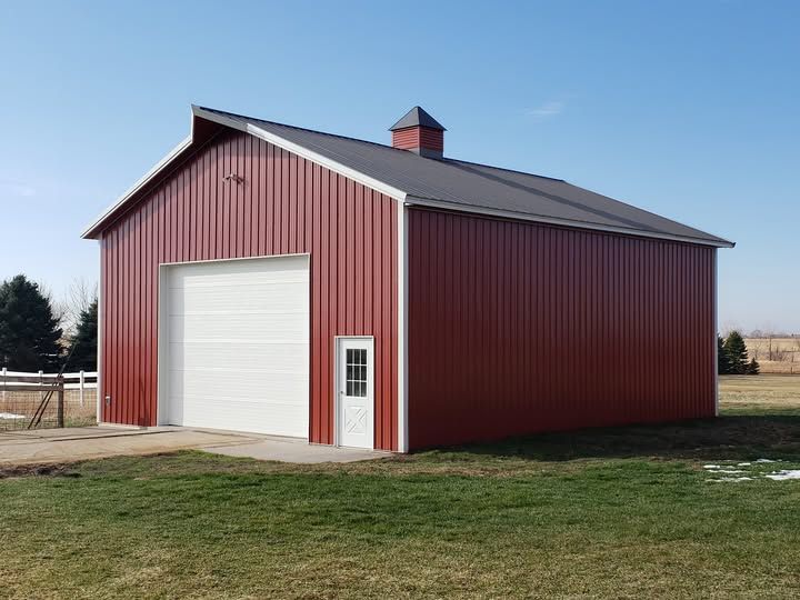 Red metal barn with white door and roof trim, set on green grass under blue sky.