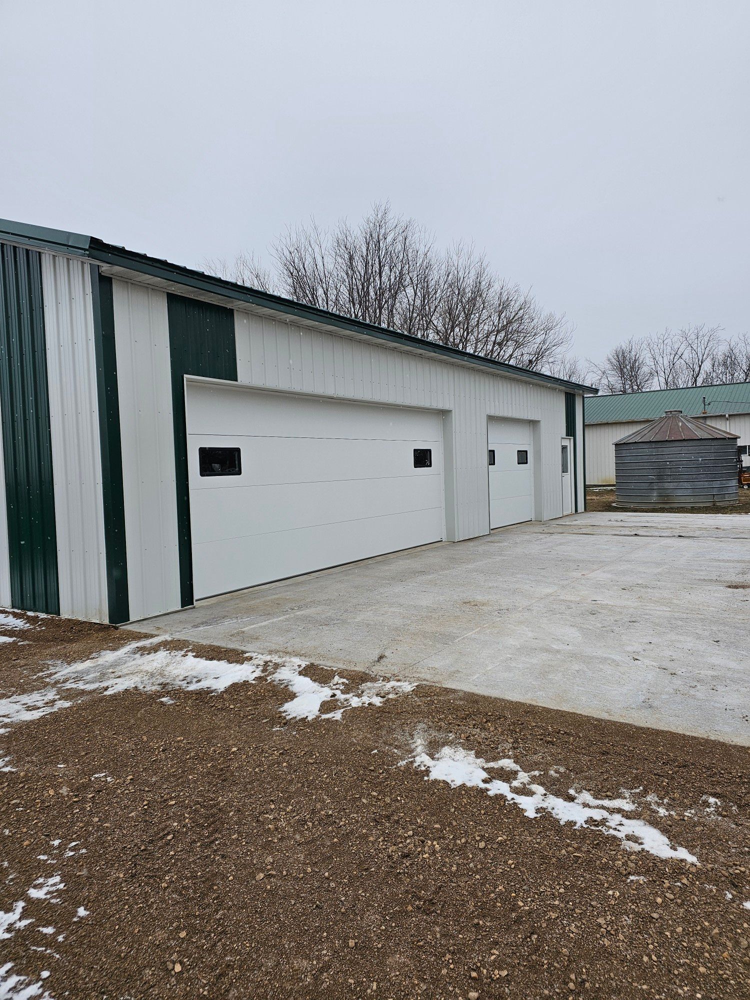White garage doors on a green and white building. Snow covers the ground.