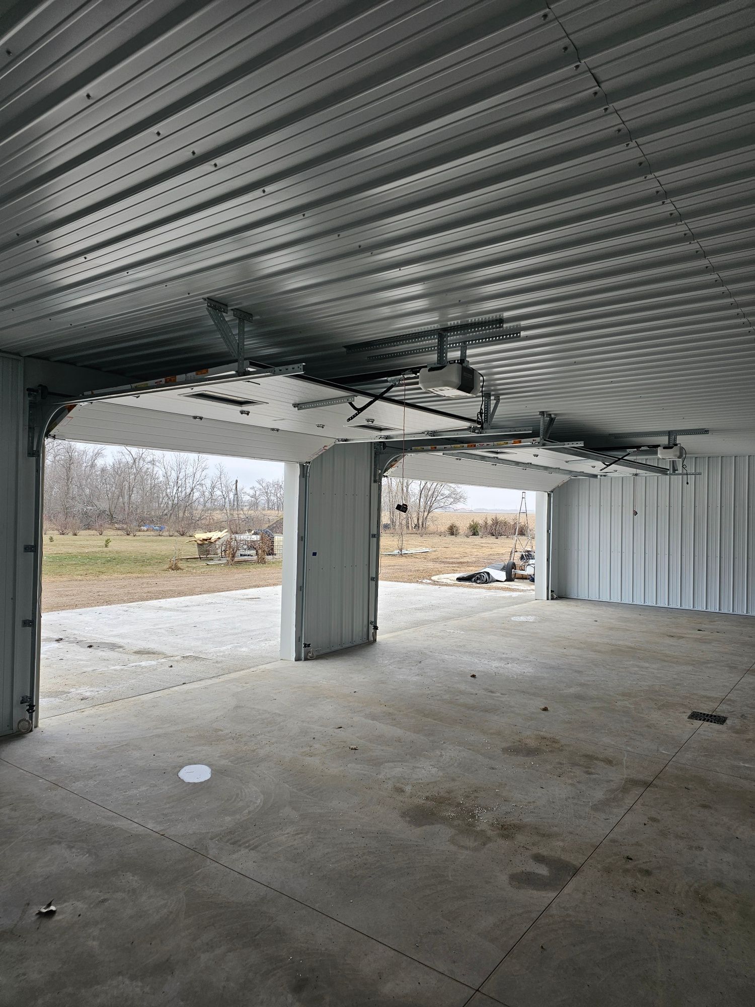 Damaged garage door, white walls, and concrete floor. Exterior view of open door and yard.